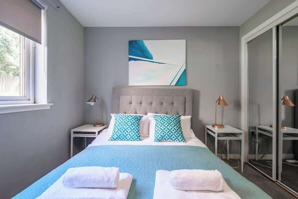 A bedroom with a bed, two bedside tables, a window, and a wall-mounted artwork.