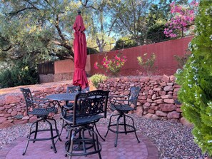 Une terrasse extérieure avec un mur en pierre, un parasol rouge et des chaises en métal.