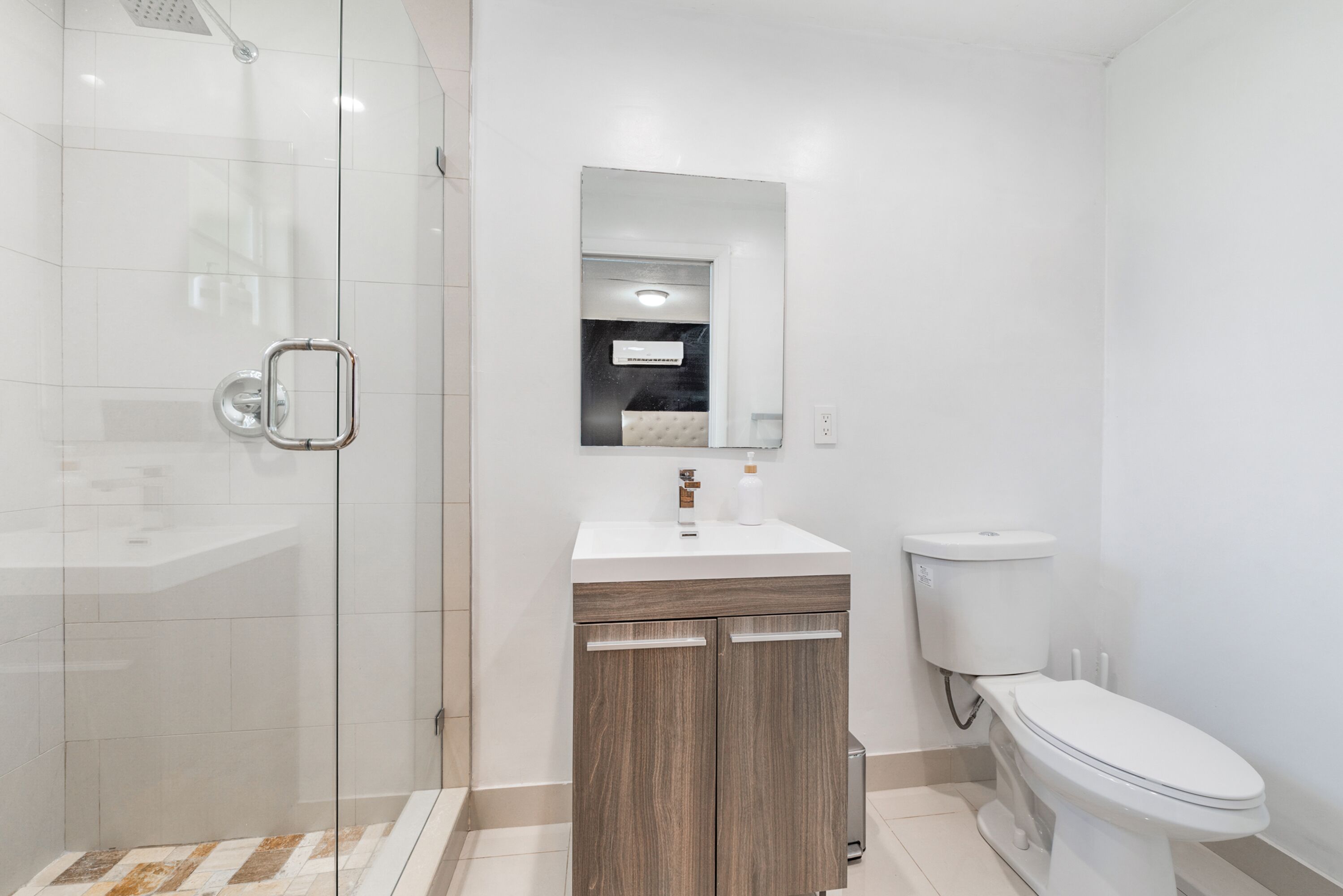 A modern bathroom with a glass shower enclosure, a wooden vanity, a white sink, and a toilet.