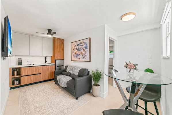 A modern kitchen with white cabinets, a grey sofa, and a glass dining table.
