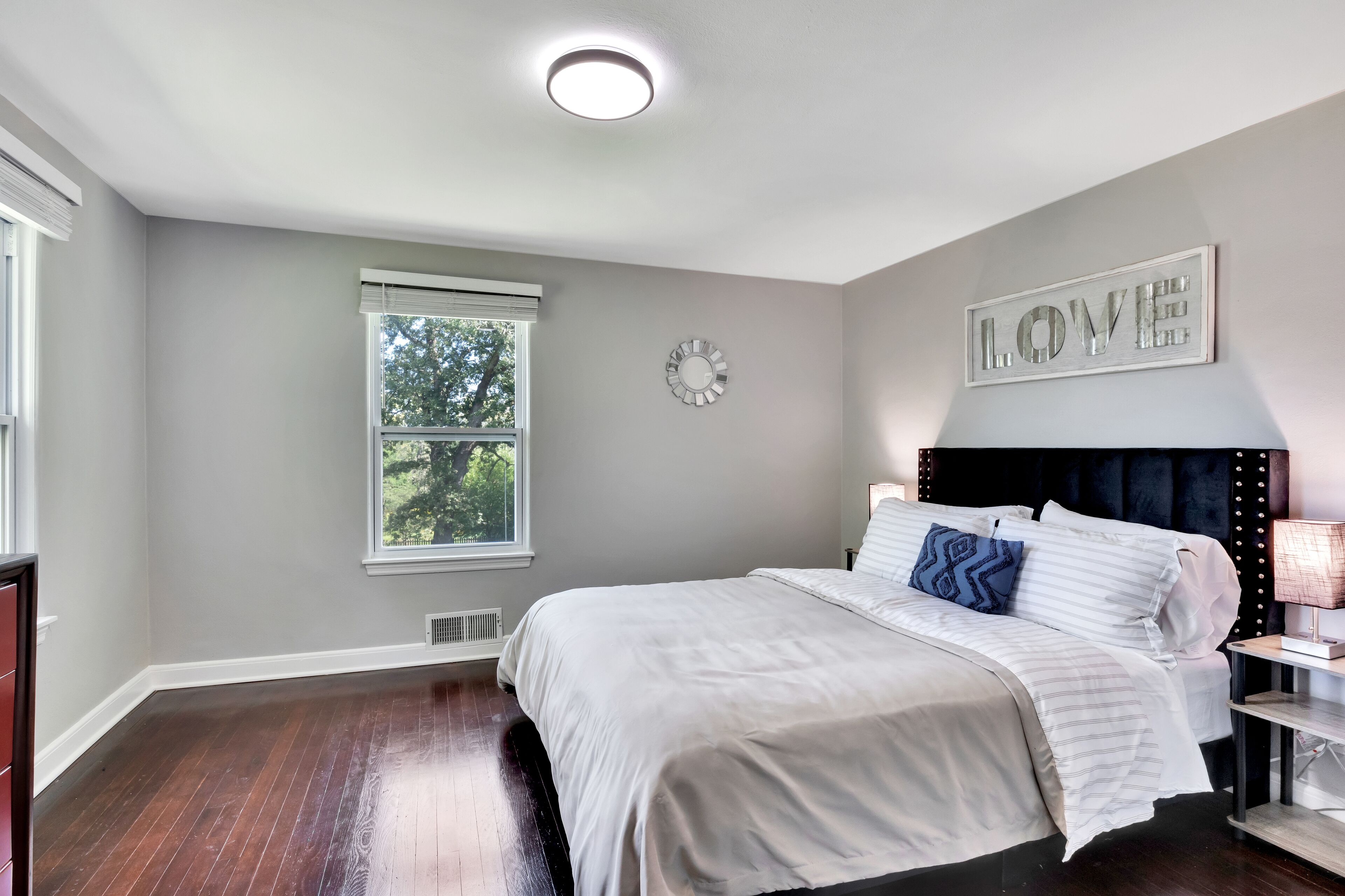 Une chambre à coucher avec un lit, une table de chevet, une horloge murale et une fenêtre.