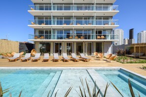 Un hotel moderno de varios pisos con piscina en la azotea, tumbonas y vistas del horizonte urbano.