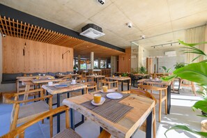 Un café amplio con mesas y sillas de madera, un diseño moderno de techo y grandes ventanales que dejan entrar la luz natural.
