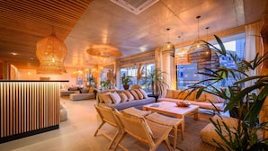 A modern lounge area with a wooden reception desk, comfortable seating, and large windows offering a city view. - Ambar Hotel (Punta del Este)