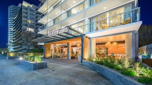A modern hotel with a glass facade, outdoor seating area, and a well-lit entrance. - Ambar Hotel (Punta del Este)