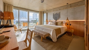 A modern hotel room with a large bed, a desk with a computer, a chair, and a view of the city through large windows. - Ambar Hotel (Punta del Este)