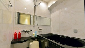 Un bagno moderno con una grande vasca da bagno nera, uno specchio sopra il lavabo e due bottiglie rosse sul ripiano.