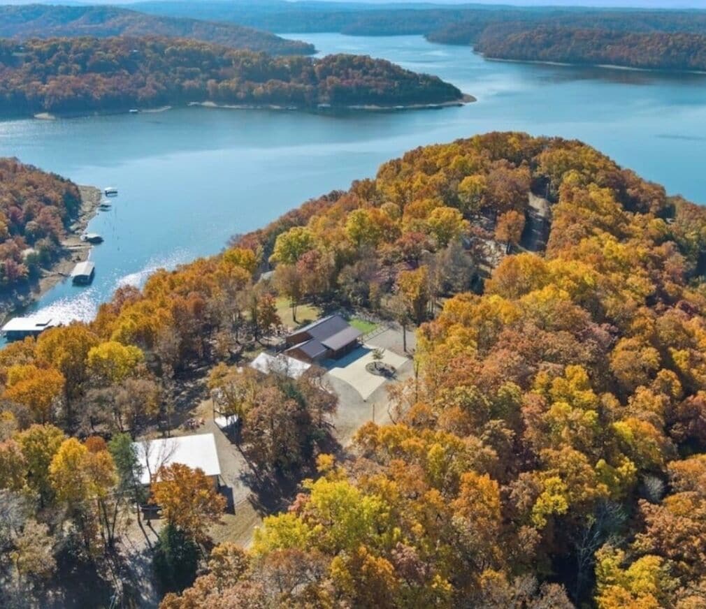 Luftaufnahme eines Anwesens am Seeufer, mit einem Haus, umgeben von dichtem Herbstlaub.