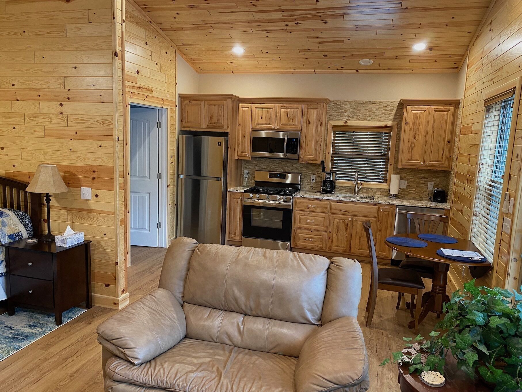 A cozy cabin interior with a leather chair, wooden walls, a kitchenette, and a dining area.