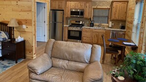 A cozy cabin interior with a leather chair, wooden walls, a kitchenette, and a dining area. - Eureka Springs, AR. Cozy log cabin studio, sleeps 2-4.Lake view- 15 min to town  (Eureka Springs)
