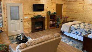 A cozy room with a fireplace, a TV, a bed, a sofa, and a ceiling fan. - Eureka Springs, AR. Cozy log cabin studio, sleeps 2-4.Lake view- 15 min to town  (Eureka Springs)