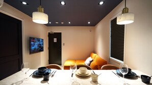 Ein Essbereich mit einem Tisch für vier Personen, einer Couch mit orangefarbenen Kissen und einem an der Wand montierten Fernseher.