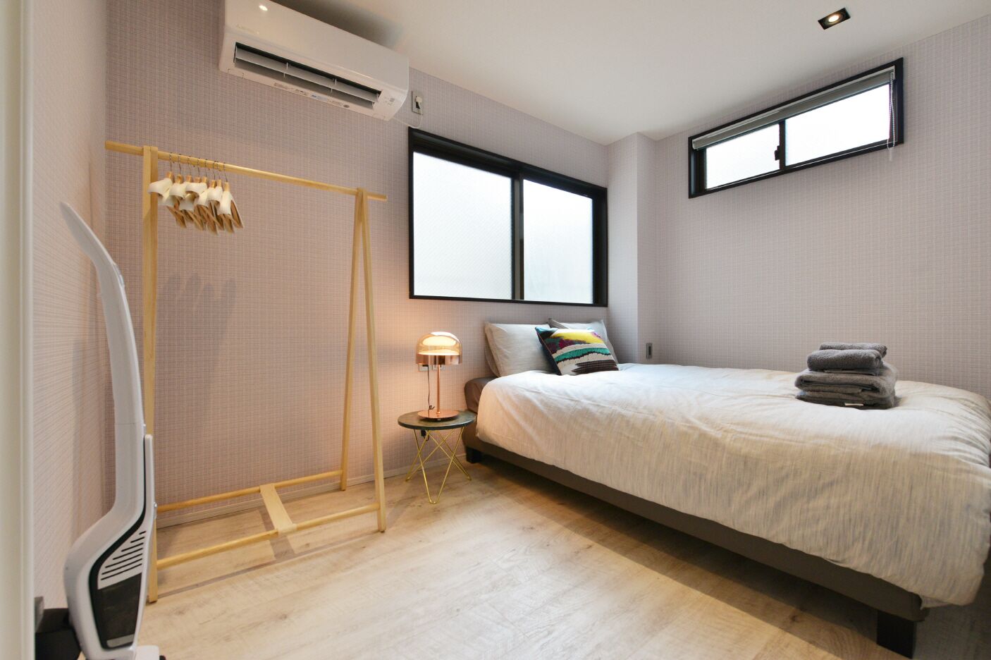 Un dormitorio moderno con una cama, una mesita de noche pequeña, un calentador y una ventana.
