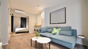 Una sala de estar moderna y bien iluminada, con un sofá, una mesa de centro y una cama al fondo.