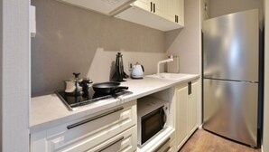 Una cocina compacta con armarios blancos, un refrigerador de acero inoxidable, una estufa y un microondas.