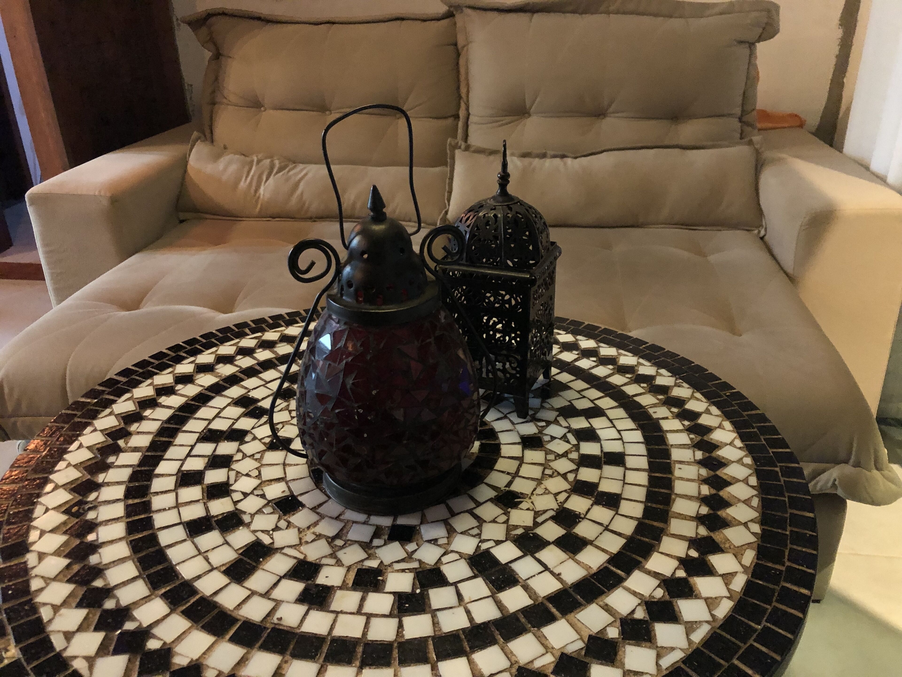 Une table ronde ornée d’un motif en mosaïque, une lanterne décorative et un canapé moelleux en arrière-plan.