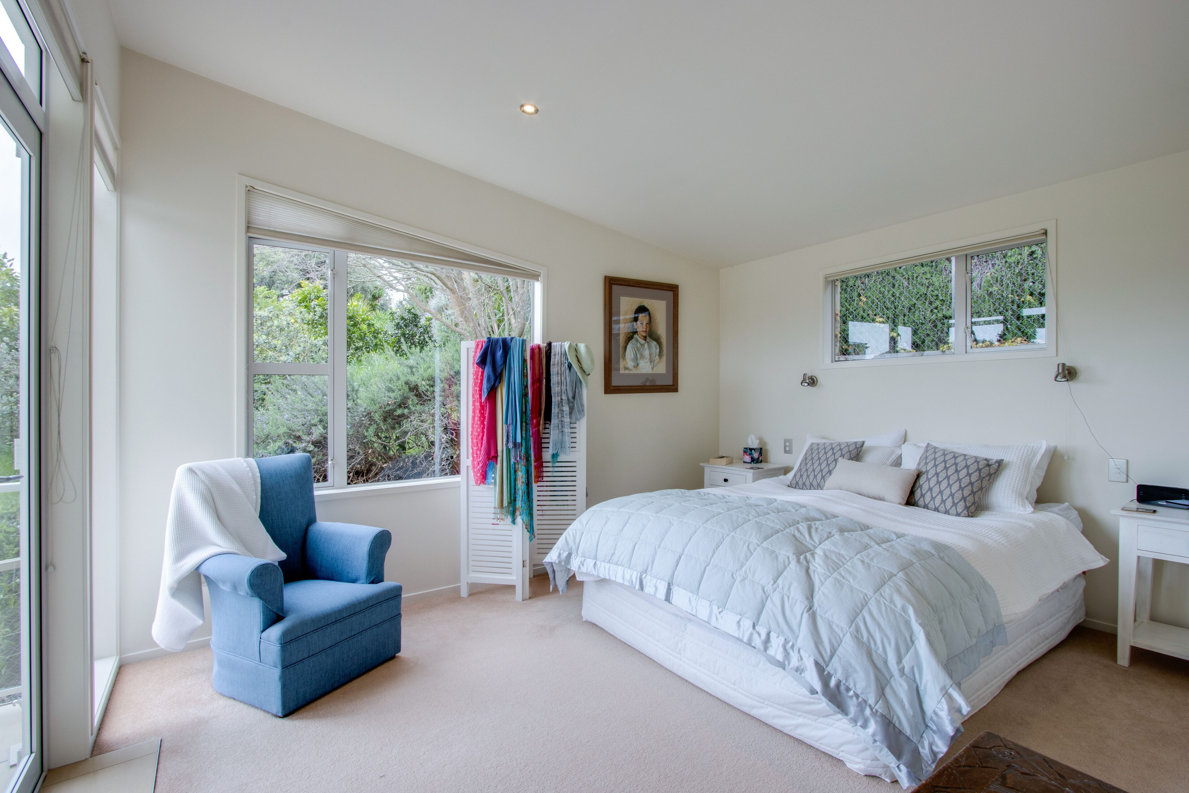 Une chambre à coucher avec un grand lit, une chaise, une armoire et deux fenêtres.