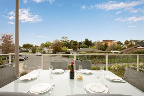 A dining table set for four with wine and glasses, overlooking a street with cars and houses.