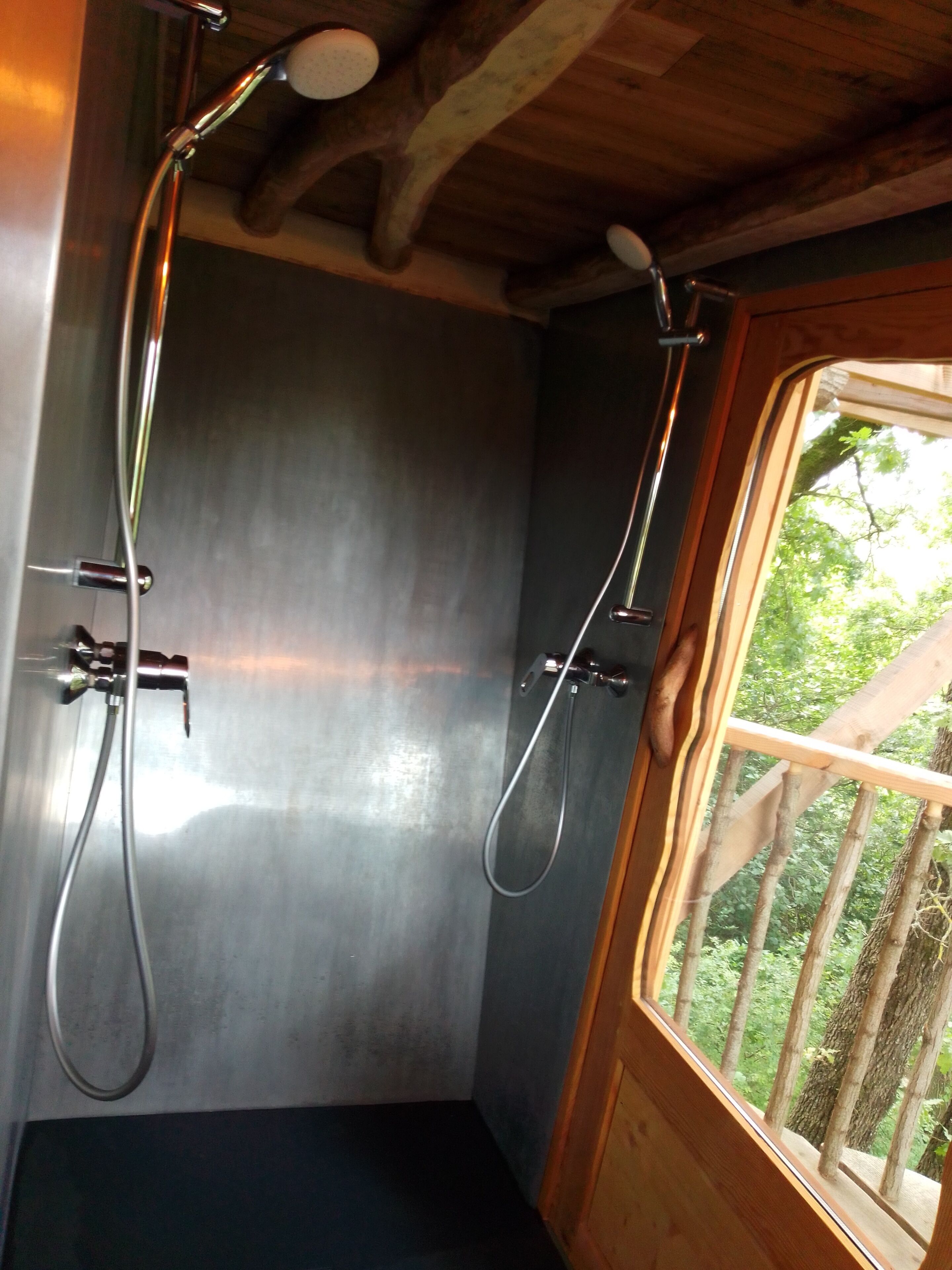 A shower area with a wooden ceiling and a window overlooking greenery.