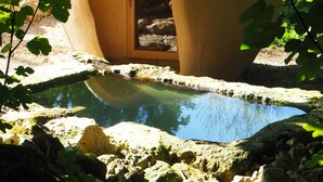A dome-shaped structure with an open entrance, surrounded by a natural setting with rocks and foliage. - Cabane perchée / sauna & cold bath / shared natural swimming pool (L'Isle-Bouzon)