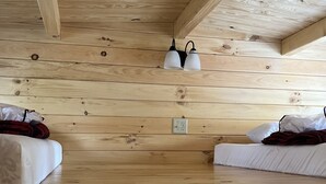 Interior d'una cabana de fusta amb dos llits, una làmpada al sostre i una presa de corrent.