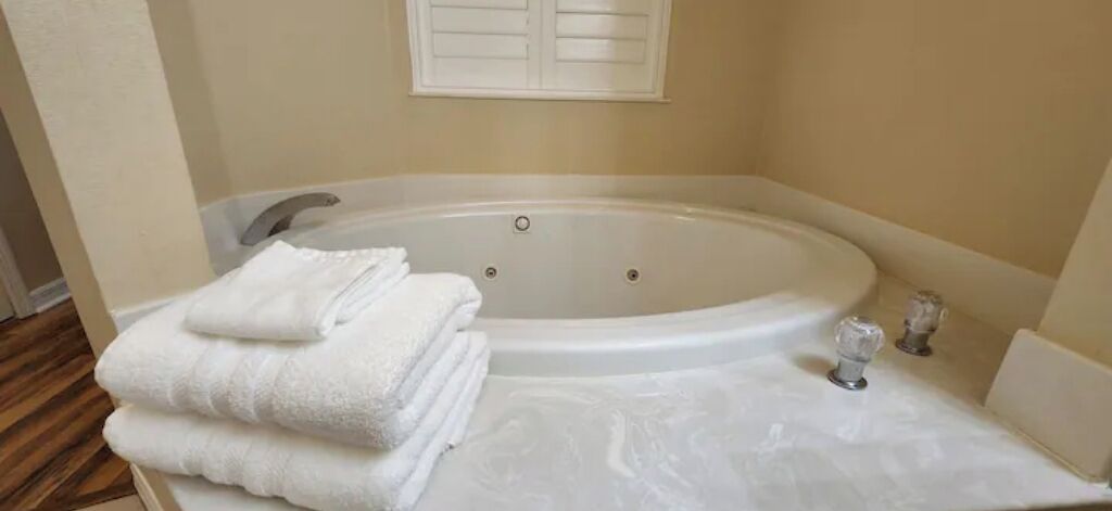 A bathroom with a large bathtub, a white towel stack, and a white sink.