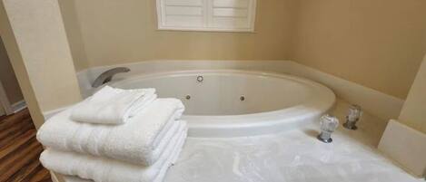 A bathroom with a large bathtub, a white towel stack, and a white sink.