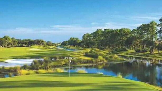 Golfkenttä, jossa on lampi, puita ja kirkas taivas.