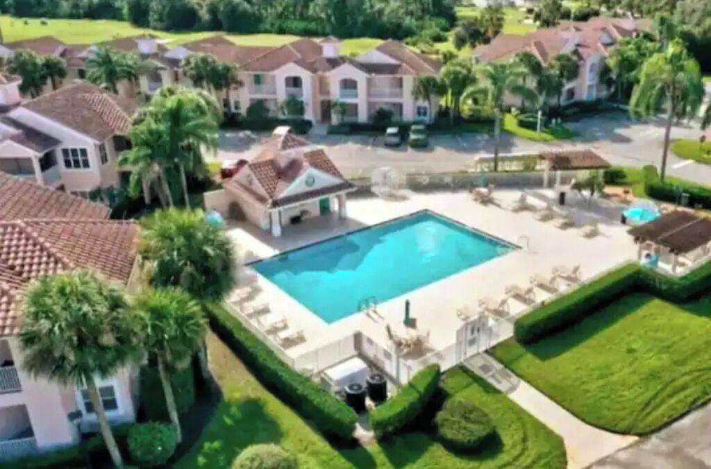 Zona residencial con piscina rodeada de céspedes cuidados y palmeras.