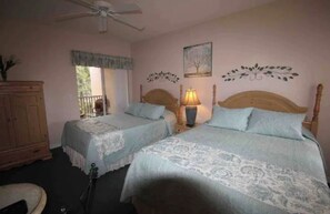 Une chambre avec deux lits, un ventilateur de plafond, une table de chevet avec une lampe, une armoire en bois et une fenêtre donnant sur un beau paysage.
