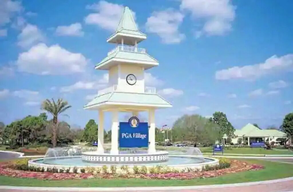 Ein Pavillon mit einer Uhr, umgeben von einem kreisförmigen Wasserspiel und einem Schild mit der Aufschrift 'PGA Village'.