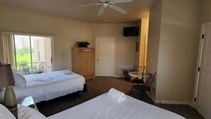 A hotel room with two beds, a ceiling fan, a TV, a small table, and a door leading to a balcony.