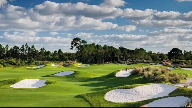 A golf course with sand bunkers and a line of trees in the background.