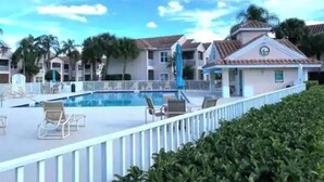 A swimming pool area with lounge chairs and umbrellas, surrounded by multi-story buildings with a tiled roof.