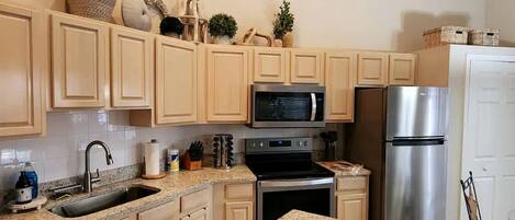 A kitchen with light-colored cabinets, stainless steel appliances, a granite countertop, and decorative items on the upper cabinets.