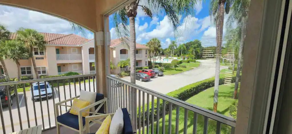 A balcony with a view of a residential street, palm trees, and a clear sky.