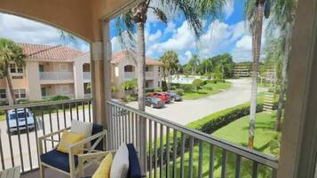 A balcony with a view of a residential street, palm trees, and a clear sky.