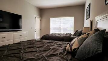 A bedroom with a large bed, a television on a dresser, and a window with blinds.