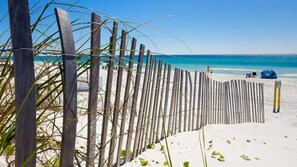 A beach with a wooden fence, a clear blue sky, and a calm sea.