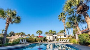 A pool area with lounge chairs, palm trees, and a building in the background. - Walk to the Beach | Community Pool & Private Fenced Yard (Miramar Beach)