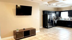 A modern kitchen with a flat-screen TV, dark cabinetry, and a tiled floor. - Gated Parking/4 Bedroom-5 bed -2bath Entire Home (Eagle Pass)