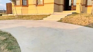 A yellow building with a concrete driveway and a small lawn area. - Gated Parking/4 Bedroom-5 bed -2bath Entire Home (Eagle Pass)