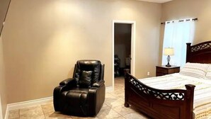 A bedroom with a wooden bed, a massage chair, and a nightstand with a lamp. - Gated Parking/4 Bedroom-5 bed -2bath Entire Home (Eagle Pass)
