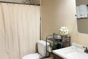 Ein Badezimmer mit Toilette, Waschbecken, einer Duschkabine sowie einem Regal mit Pflanze und Vase.