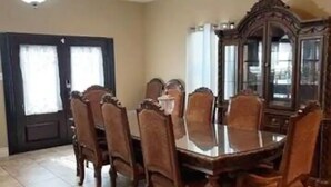A dining room with a large wooden table and matching chairs, a dark wooden cabinet, and a door with a window. - Gated Parking/4 Bedroom-5 bed -2bath Entire Home (Eagle Pass)