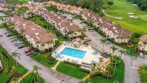 Una zona residencial con varias casas de dos pisos, una piscina central y un campo de golf al fondo.
