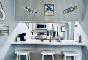A modern kitchen with a marble countertop, stainless steel appliances, and a bar area with stools.