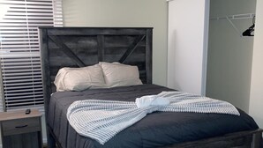 Une chambre à coucher avec un lit en bois, une table de chevet, une lampe et une fenêtre avec des stores.
