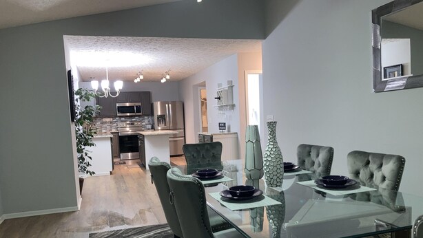 Un espace repas moderne avec une table en verre, des chaises à revêtement gris et un vase décoratif.