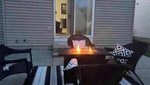 Un espace patio avec un foyer, deux chaises et une porte-fenêtre coulissante donnant sur une pièce.